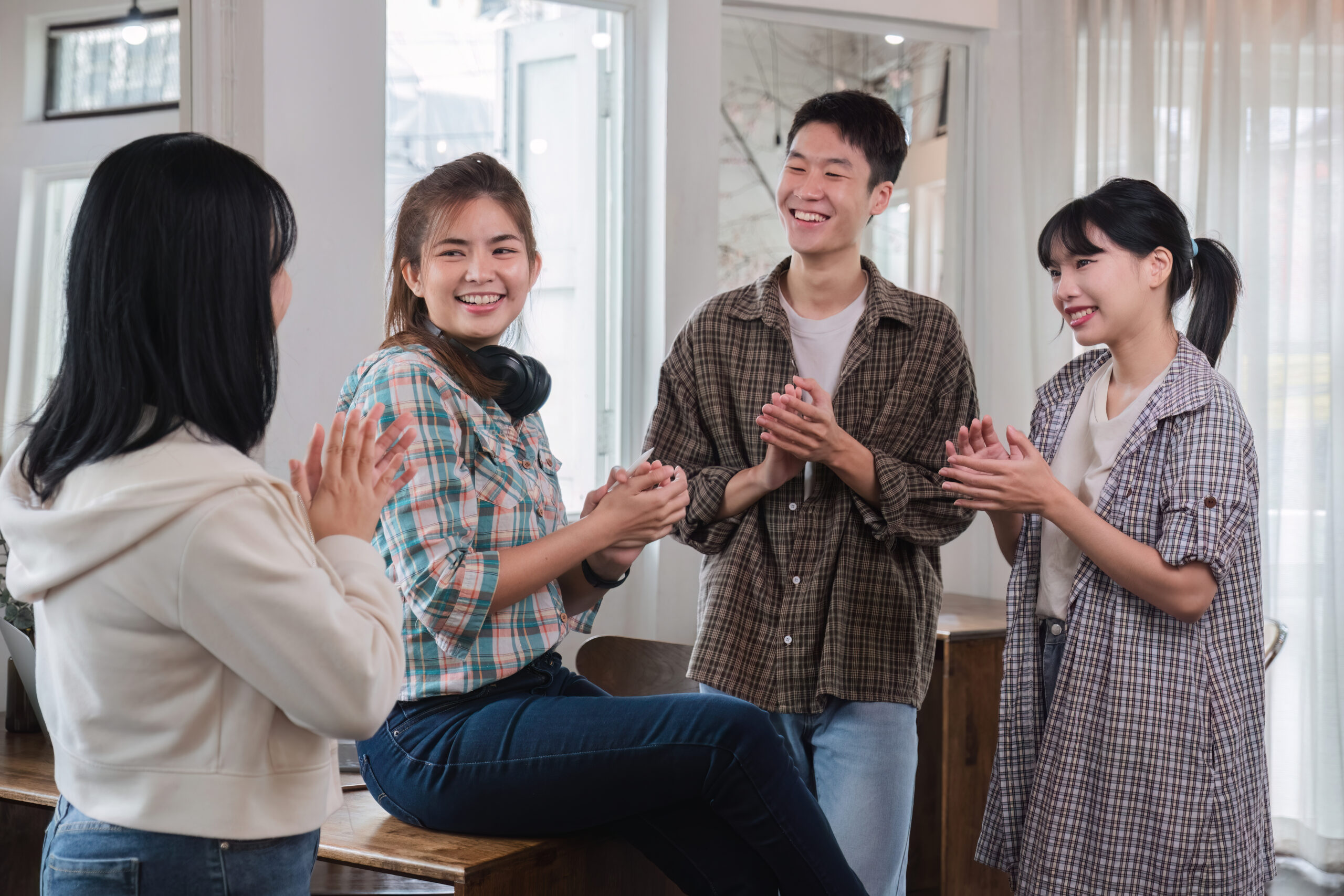 A successful businesswoman sits at a table and is surrounded by congratulating co-workers standing and applauding.